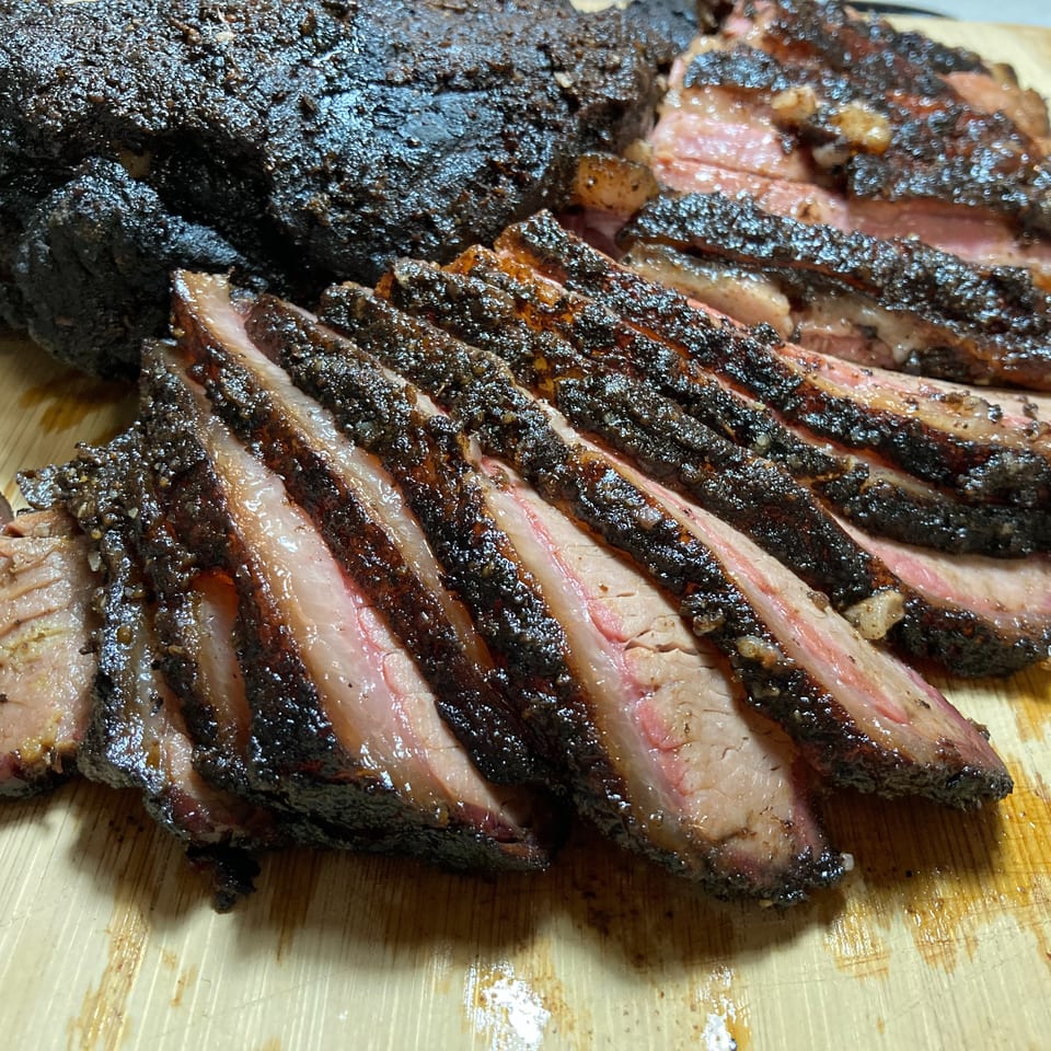 Close-up of a whole smoked brisket, partially sliced to reveal its juicy pink interior and dark bark.