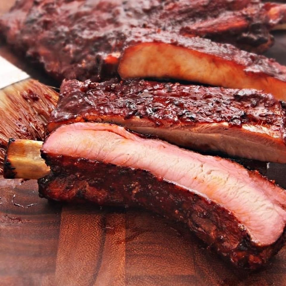 Sliced barbecue ribs with glossy smoky glaze and tender pink meat arranged on a wooden cutting board.