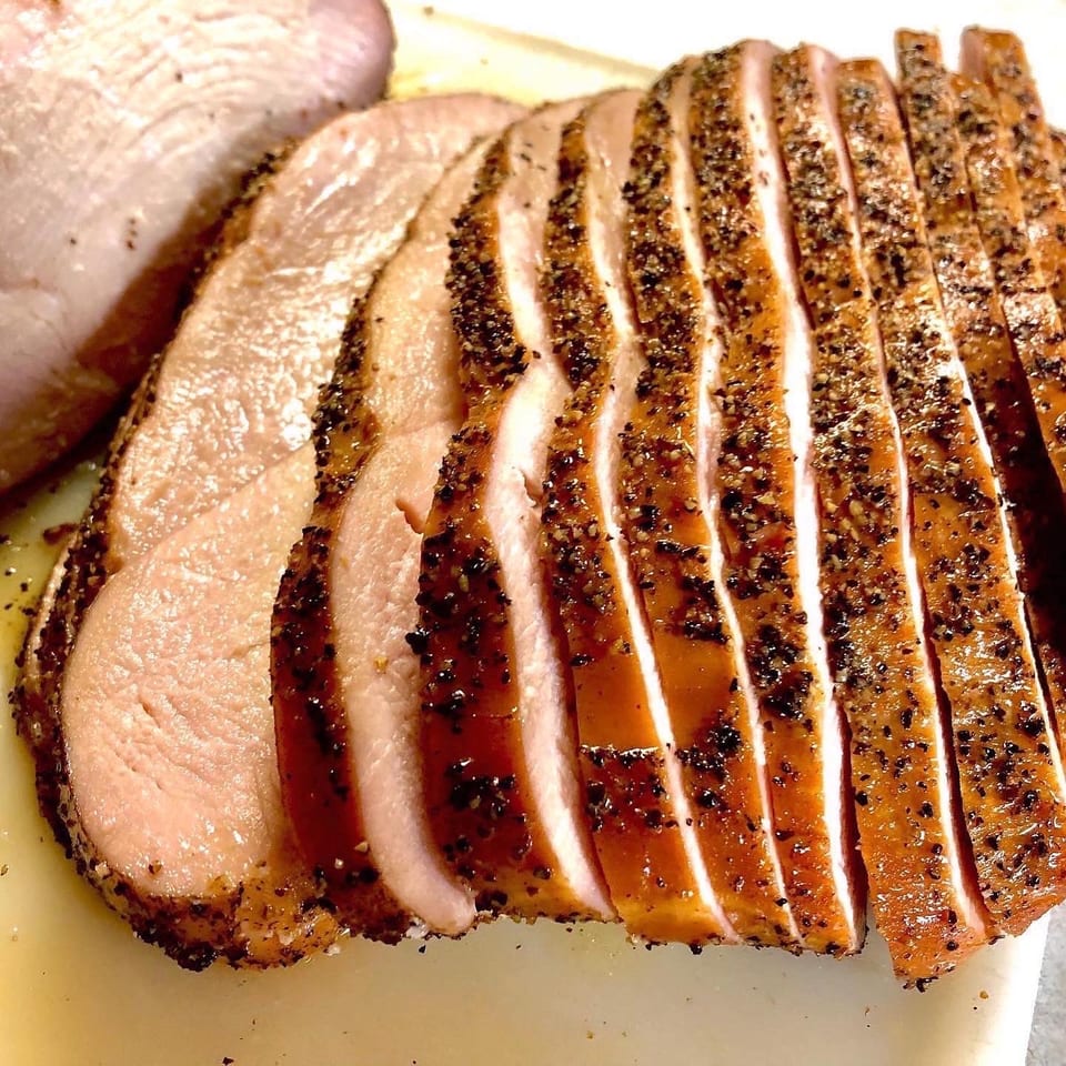 Close-up of perfectly sliced, pepper-crusted roasted pork loin on a white cutting board.
