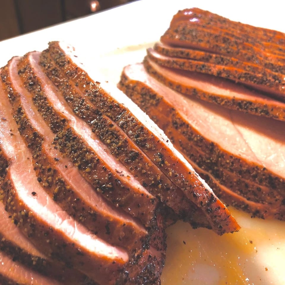 Close-up of two piles of thinly sliced, pepper-crusted meat on a white platter.