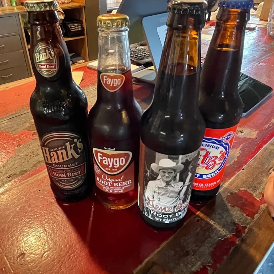 Four bottled root beers, including Hank’s, Faygo, and Fitz’s, displayed on a restaurant counter.