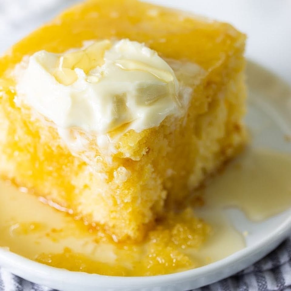 A slice of golden cornbread topped with melting butter and drizzled with honey on a white plate.